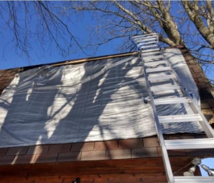 Pictured is a roof with a grey tarp on it which Servpro was tarping to eliminate any secondary damages. 